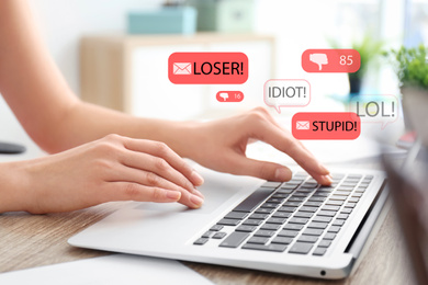 Young woman using laptop at wooden table, closeup. Cyber bullying