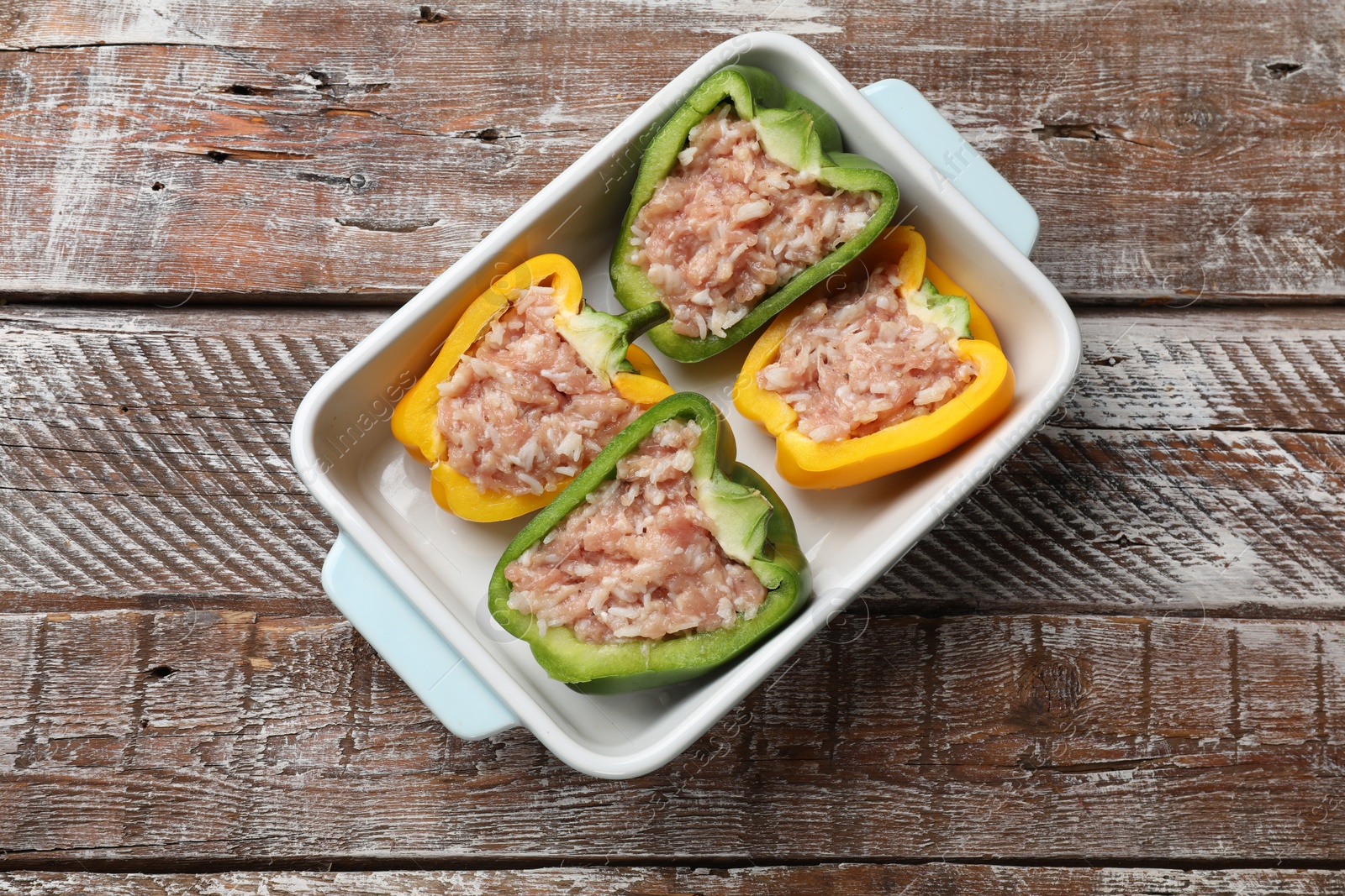 Photo of Raw stuffed peppers in dish on wooden table, top view