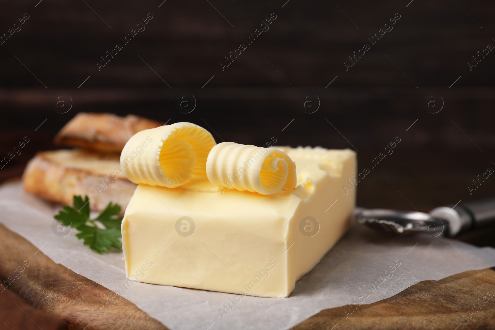 Photo of Tasty butter, slices of bread and spoon on wooden table, closeup