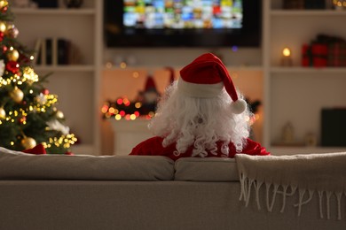 Photo of Merry Christmas. Santa Claus watching TV on sofa at home, back view