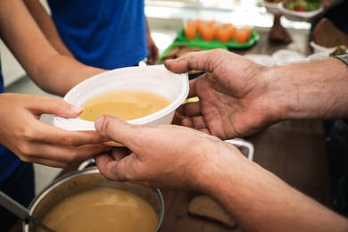 Photo of Volunteer serving food to poor people in charity centre, closeup