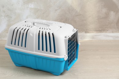 Photo of Light blue pet carrier on floor near beige wall, space for text
