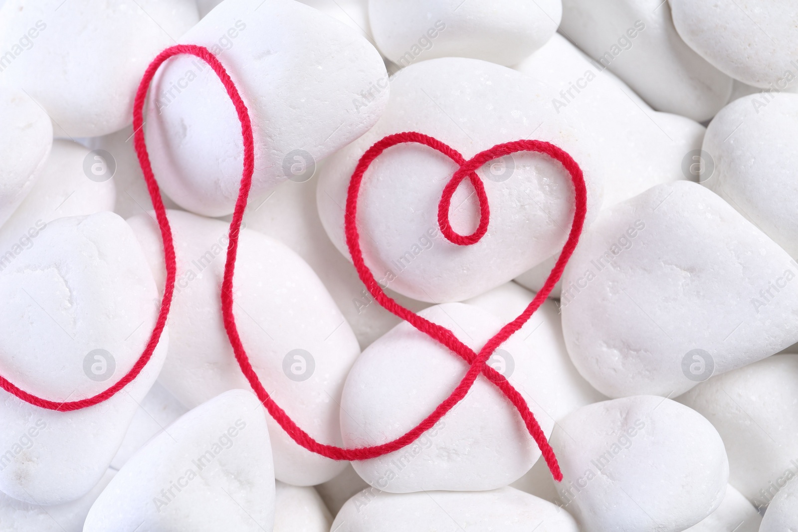 Photo of Heart made of thread on white pebble stones, top view