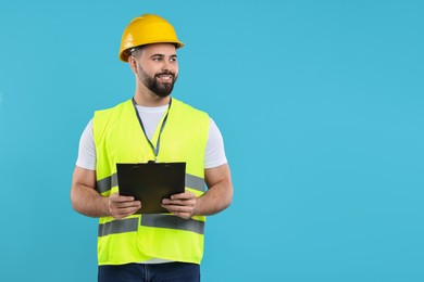 Photo of Engineer in hard hat holding clipboard on light blue background, space for text