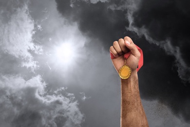 Image of Winner raising hand with gold medal up to stormy sky, closeup. Space for text