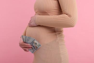 Surrogate mother. Pregnant woman with dollar banknotes on pink background, closeup