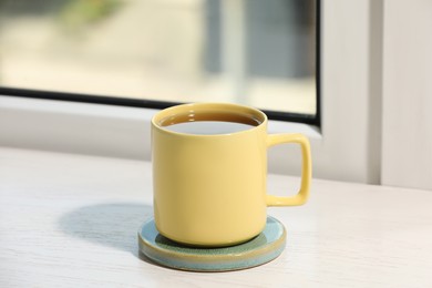 Photo of Yellow cup of tea on wooden window sill
