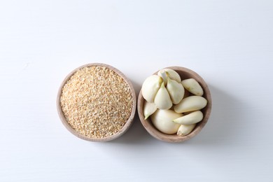 Photo of Dehydrated garlic granules and peeled cloves on white table, flat lay