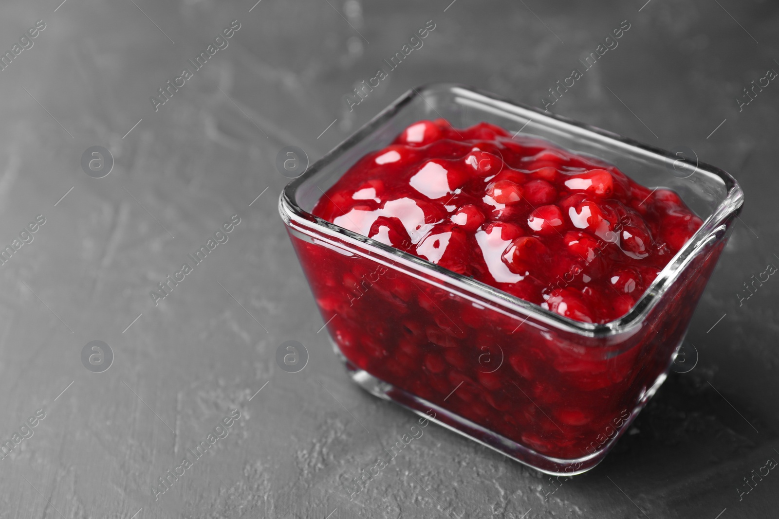 Photo of Fresh cranberry sauce in glass bowl on gray textured table, closeup. Space for text