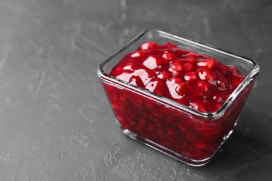 Fresh cranberry sauce in glass bowl on gray textured table, closeup. Space for text