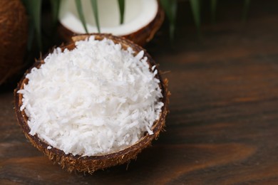 Coconut flakes in nut shell on wooden table, space for text