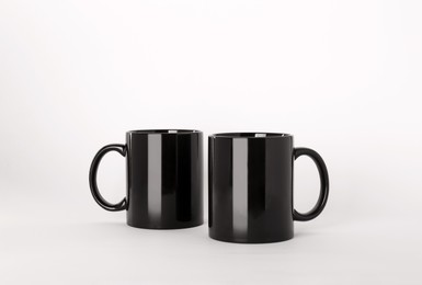 Photo of Blank black ceramic mugs on light background