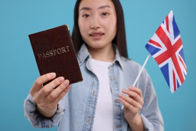 Photo of Immigration to United Kingdom. Happy woman with passport and flag on light blue background, selective focus