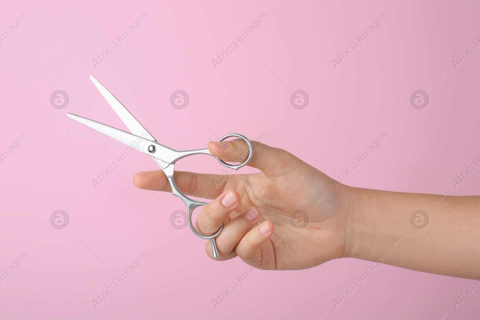 Photo of Hairdresser holding professional scissors on pink background, closeup. Haircut tool