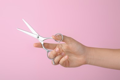 Hairdresser holding professional scissors on pink background, closeup. Haircut tool