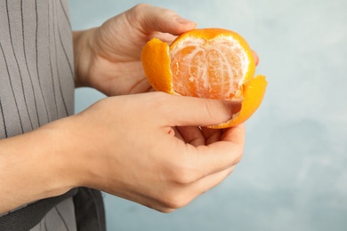Photo of Woman peeling ripe tangerine on light background, closeup