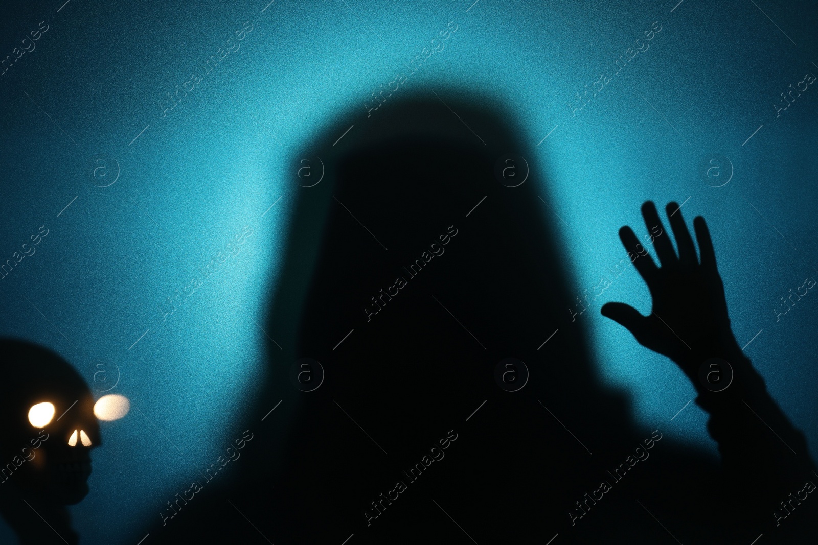 Photo of Silhouette of ghost and skull behind glass against blue background
