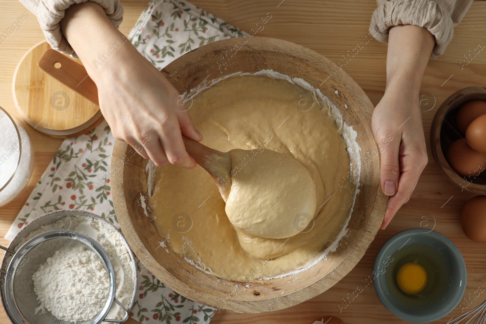 Photo of Woman kneading dough with spoon in bowl at wooden table, top view
