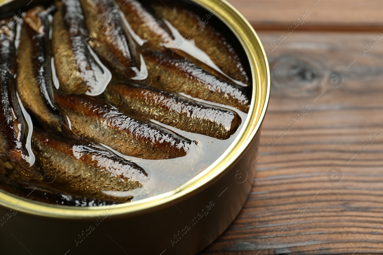 Photo of Open tin can of sprats on wooden table, closeup