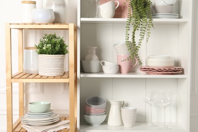 Photo of Different clean dishware and houseplants on shelves in cabinet indoors