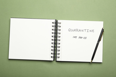 Open notebook and pen on green background, top view. Counting days of quarantine during coronavirus outbreak