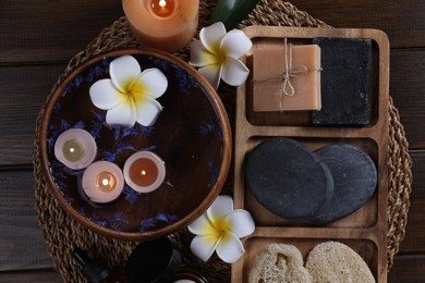 Photo of Different spa products, plumeria flowers and burning candles on wooden table, top view