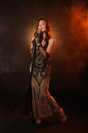 Photo of Beautiful young woman with microphone singing in color lights and smoke