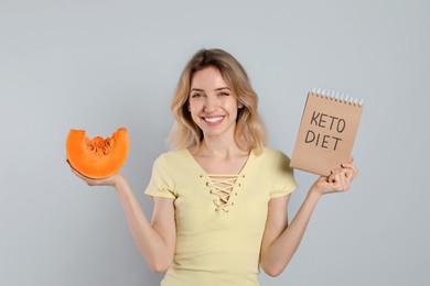 Photo of Woman holding notebook with phrase Keto Diet and pumpkin on grey background