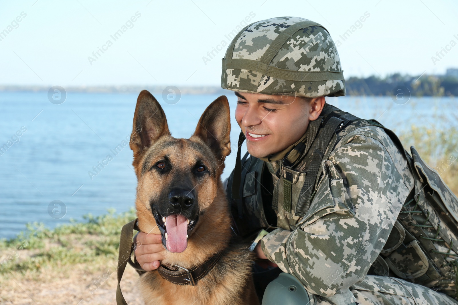 Photo of Man in military uniform with German shepherd dog near river