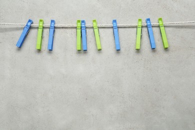 Colorful plastic clothespins and rope on light grey stone background. Space for text