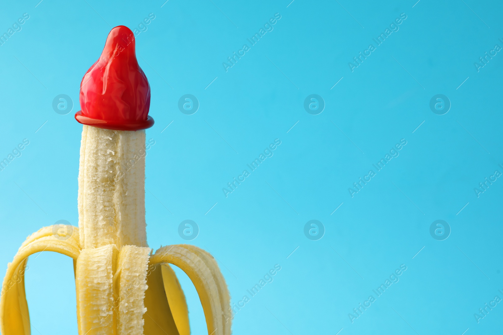 Photo of Banana with condom on light blue background, space for text. Safe sex concept