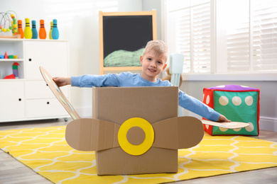 Little child playing with plane made of cardboard box at home