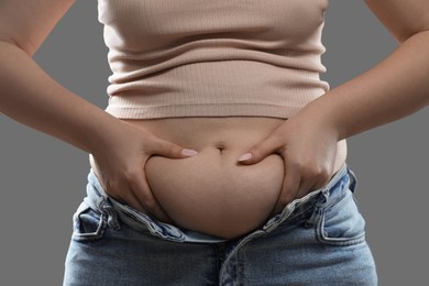 Woman touching belly fat on grey background, closeup. Overweight problem