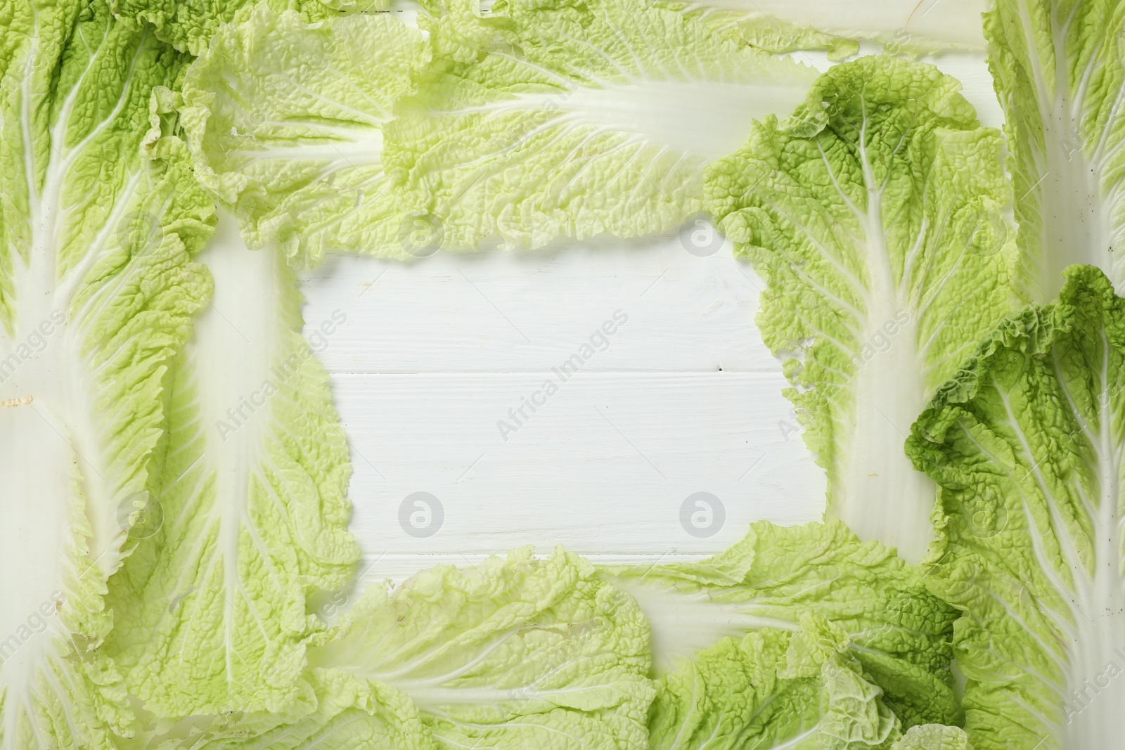 Photo of Frame with fresh ripe leaves of Chinese cabbage on white wooden table, flat lay. Space for text