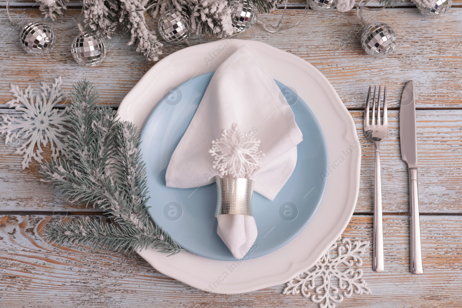 Photo of Festive place setting with beautiful dishware, cutlery and fabric napkin for Christmas dinner on light blue wooden table, flat lay