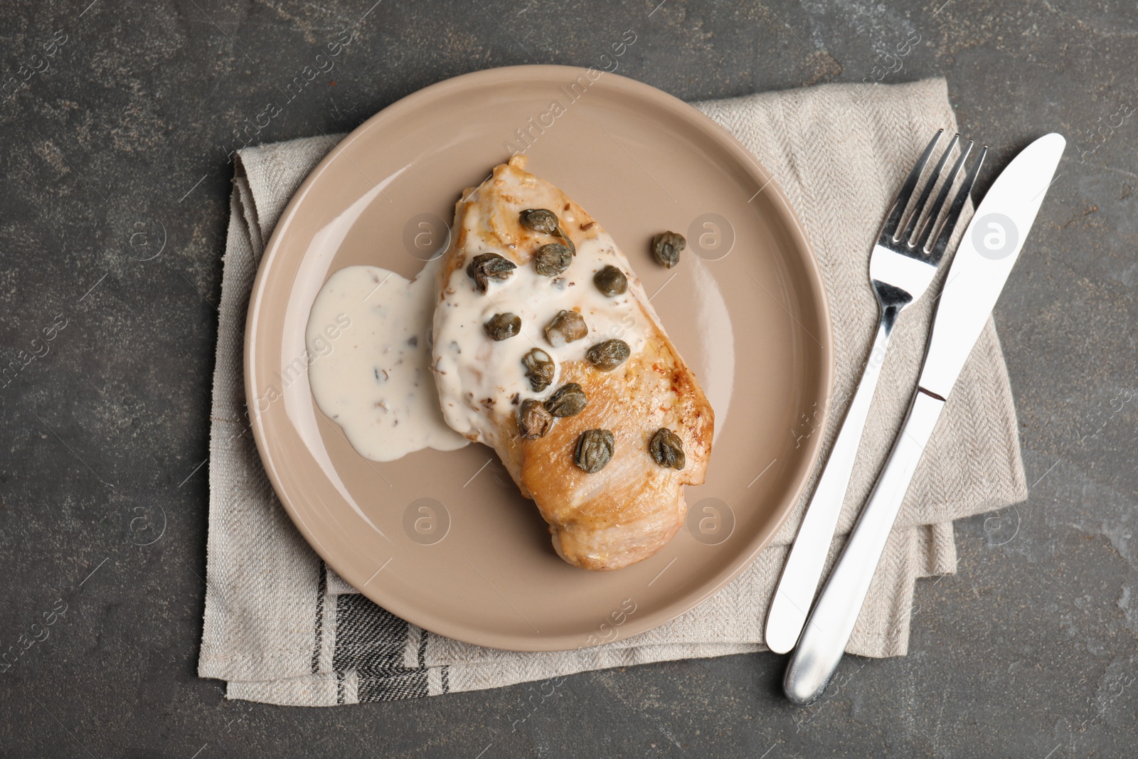 Photo of Delicious chicken fillet with capers and sauce served on grey table, flat lay