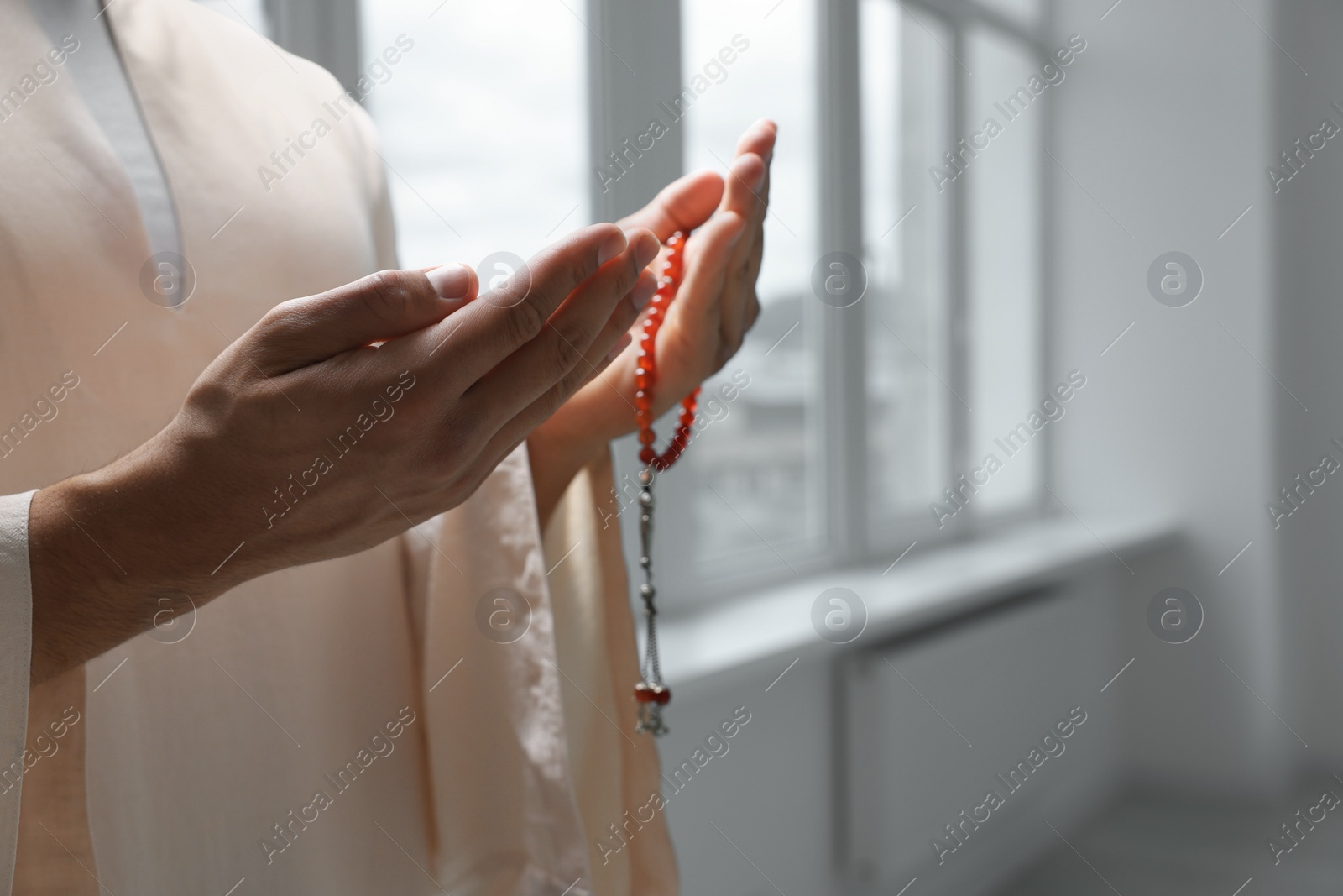 Photo of Muslim man with misbaha praying indoors, closeup. Space for text