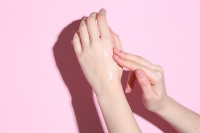 Woman applying cream on her hand against pink background, closeup