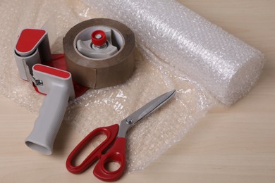 Photo of Roll of bubble wrap, scissors and adhesive tape on wooden table