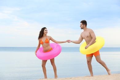 Photo of Happy young couple having fun with inflatable rings on beach near sea