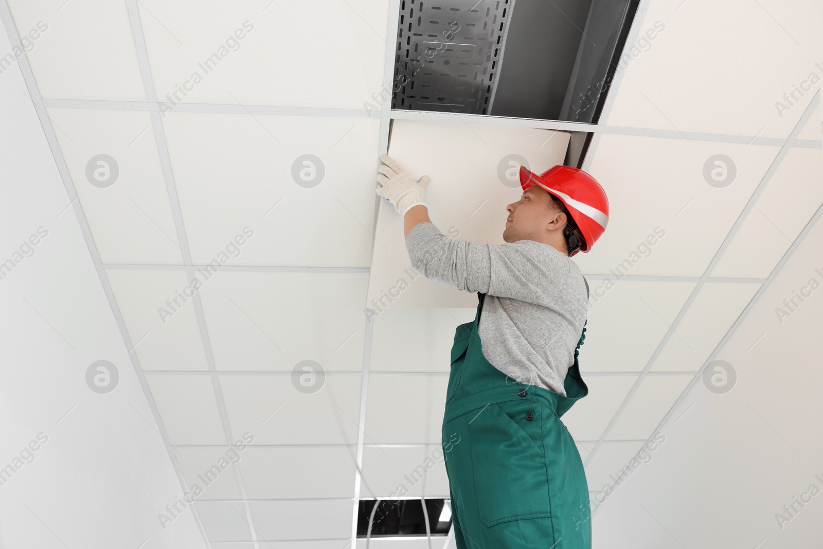 Photo of Suspended ceiling installation. Builder working with PVC tile