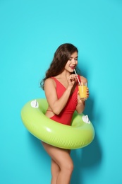 Beautiful young woman with inflatable ring and glass of cocktail on color background