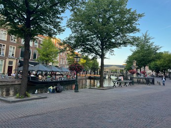 Leiden, Netherlands - August 1, 2022: Beautiful view of city street with outdoor cafe and trees along canal