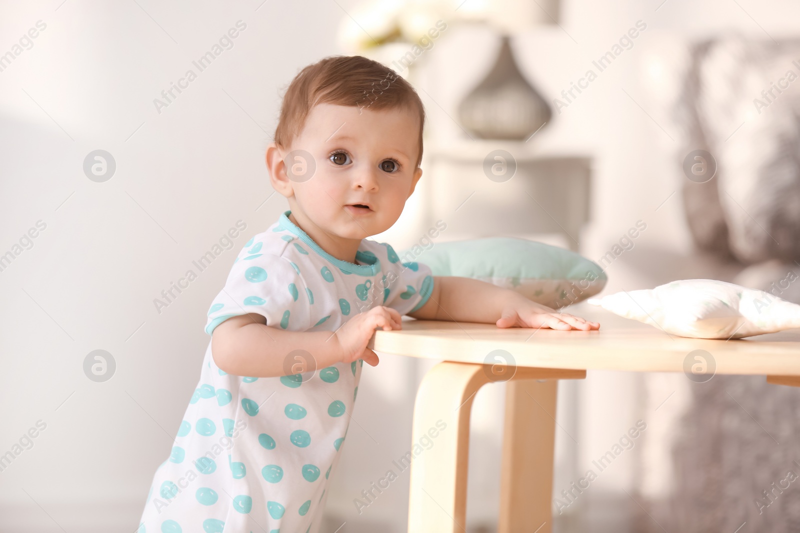 Photo of Cute baby holding on to table in living room. Learning to walk