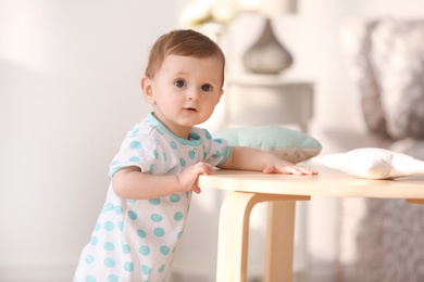 Photo of Cute baby holding on to table in living room. Learning to walk