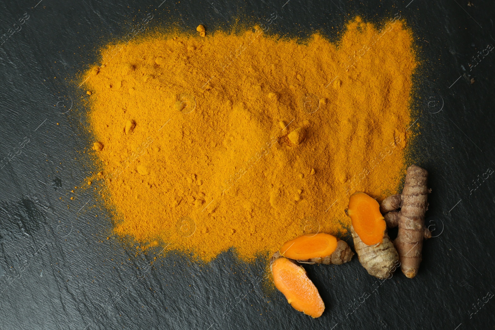 Photo of Turmeric powder and cut roots on black textured table, flat lay