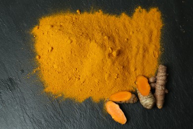 Turmeric powder and cut roots on black textured table, flat lay