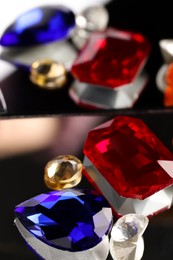 Photo of Different beautiful gemstones for jewelry on mirror surface