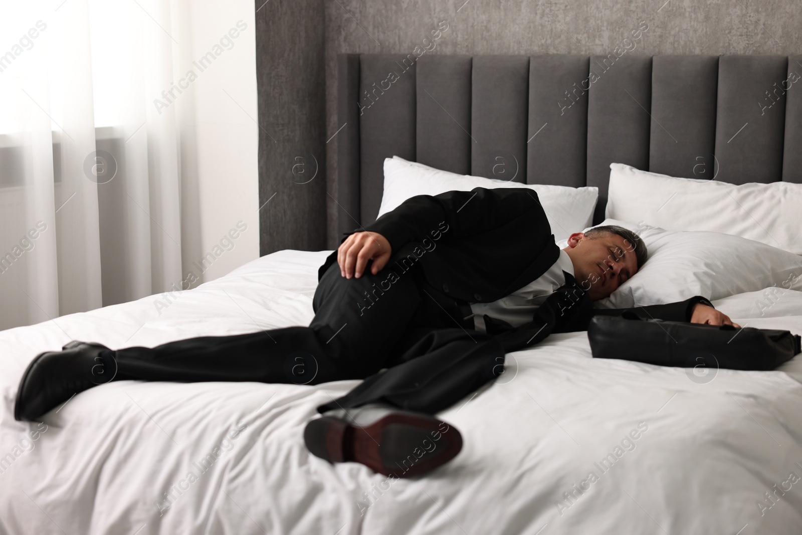 Photo of Businessman with briefcase sleeping on bed indoors