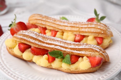 Photo of Delicious eclairs filled with cream, strawberries and mint on table, closeup